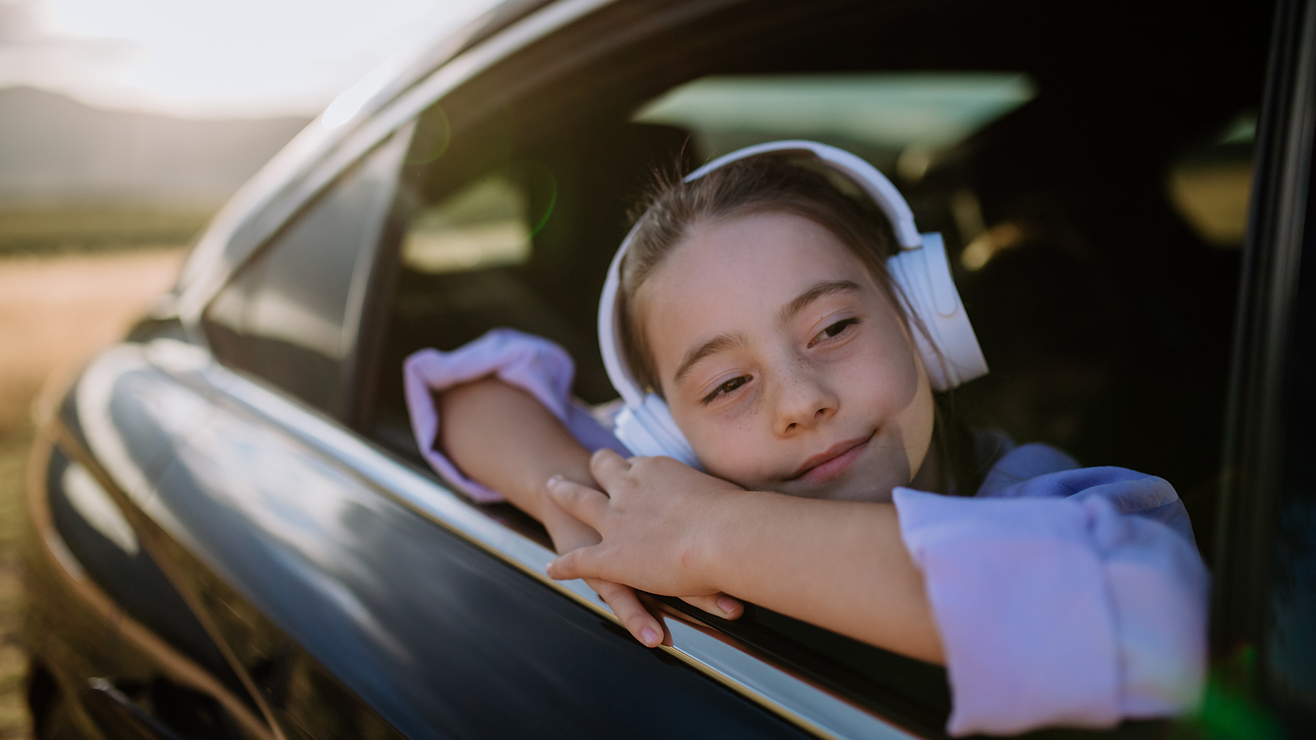 A child leaning out a car window with headphones on