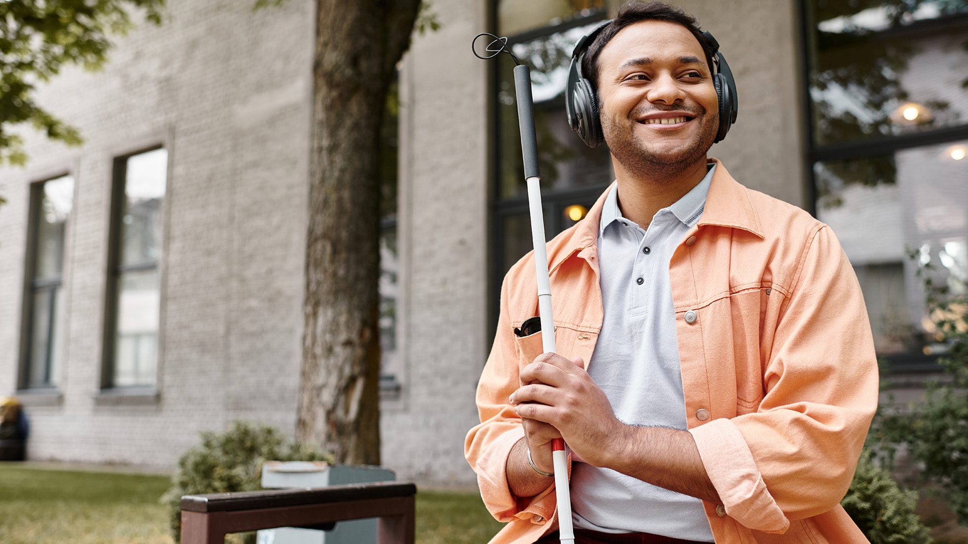 A man holding a mobility cane and wearing headphones