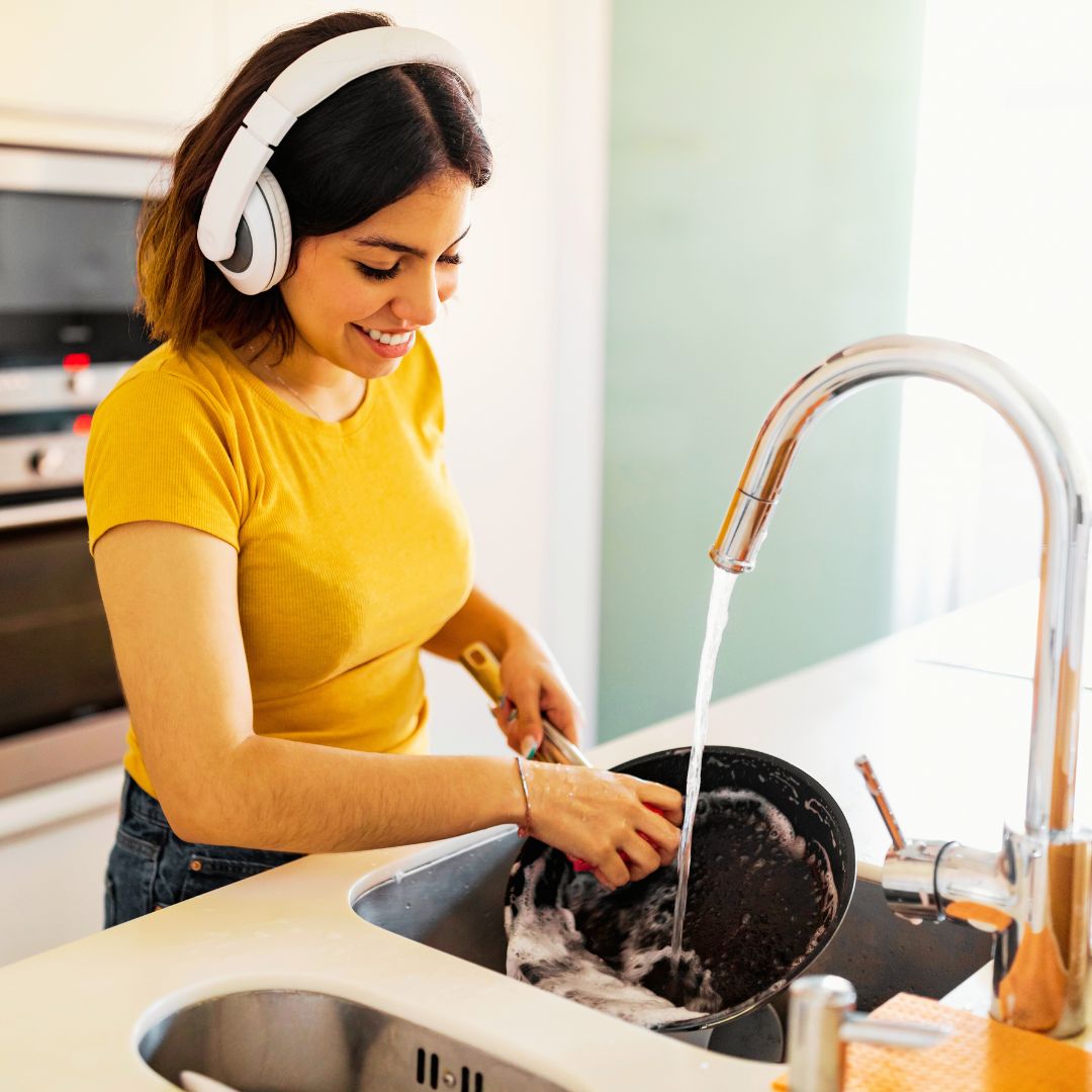 An individual washing dishes has headphones on.