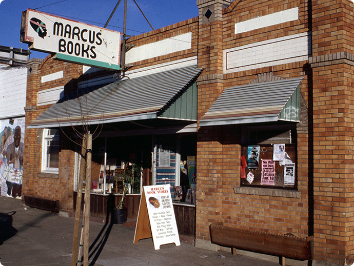 The storefront of Marcus Books: a brick building with signs in the front windows and a sandwich board on the sidewalk