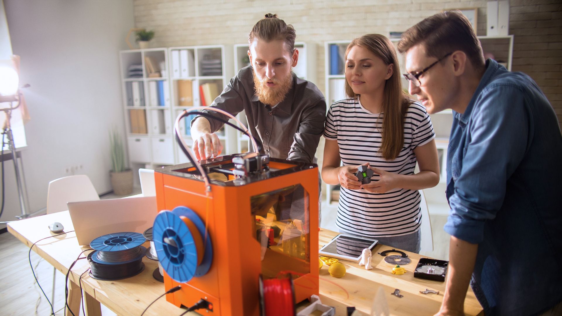 Three individuals peer into a D3 Printer