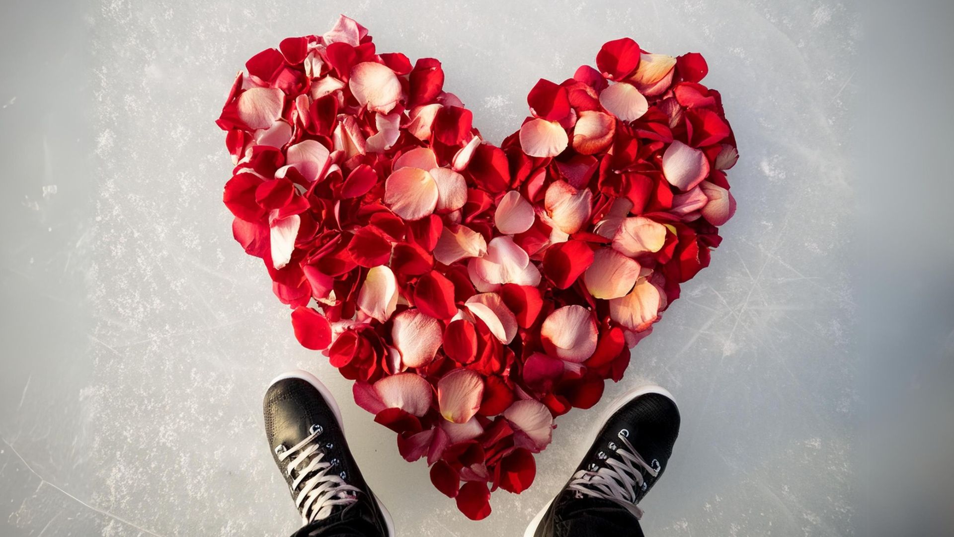 An ice rink with ice skates on either side of a heart of rose petals