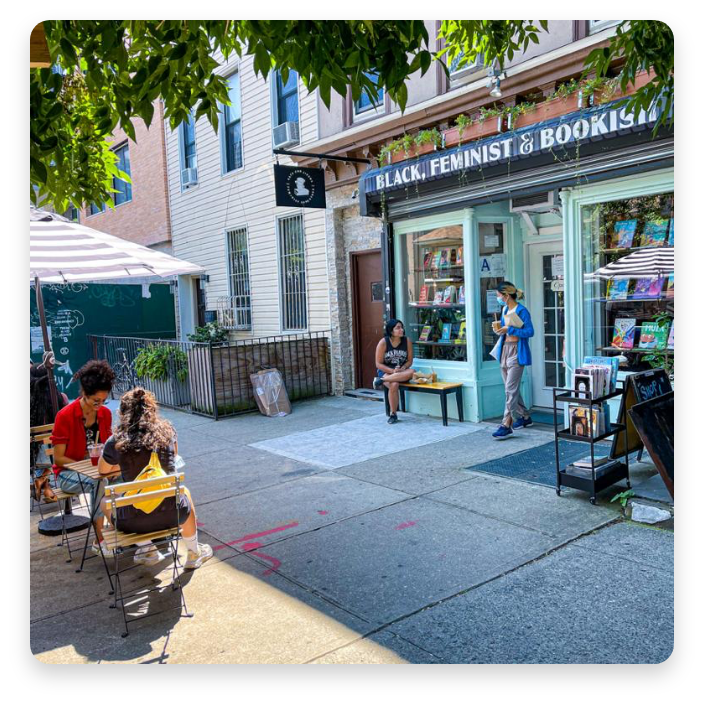 Image of Cafe con Libros bookstore in Brooklyn, with customers dining outside, and one customer exiting the store, wearing a mask.