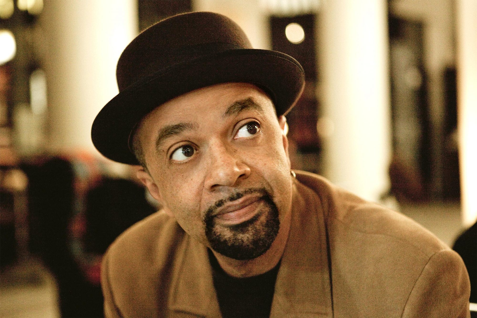 A headshot of James McBride. He looks out to the right, wearing a hat and brown jacket. 